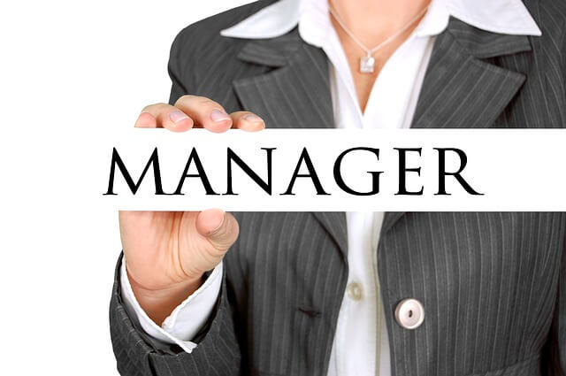 Kobieta w marynarce trzyma w ręce napis "Manager"