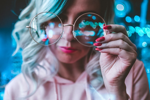 Blondwłosa kobieta trzyma okulary w dłoni